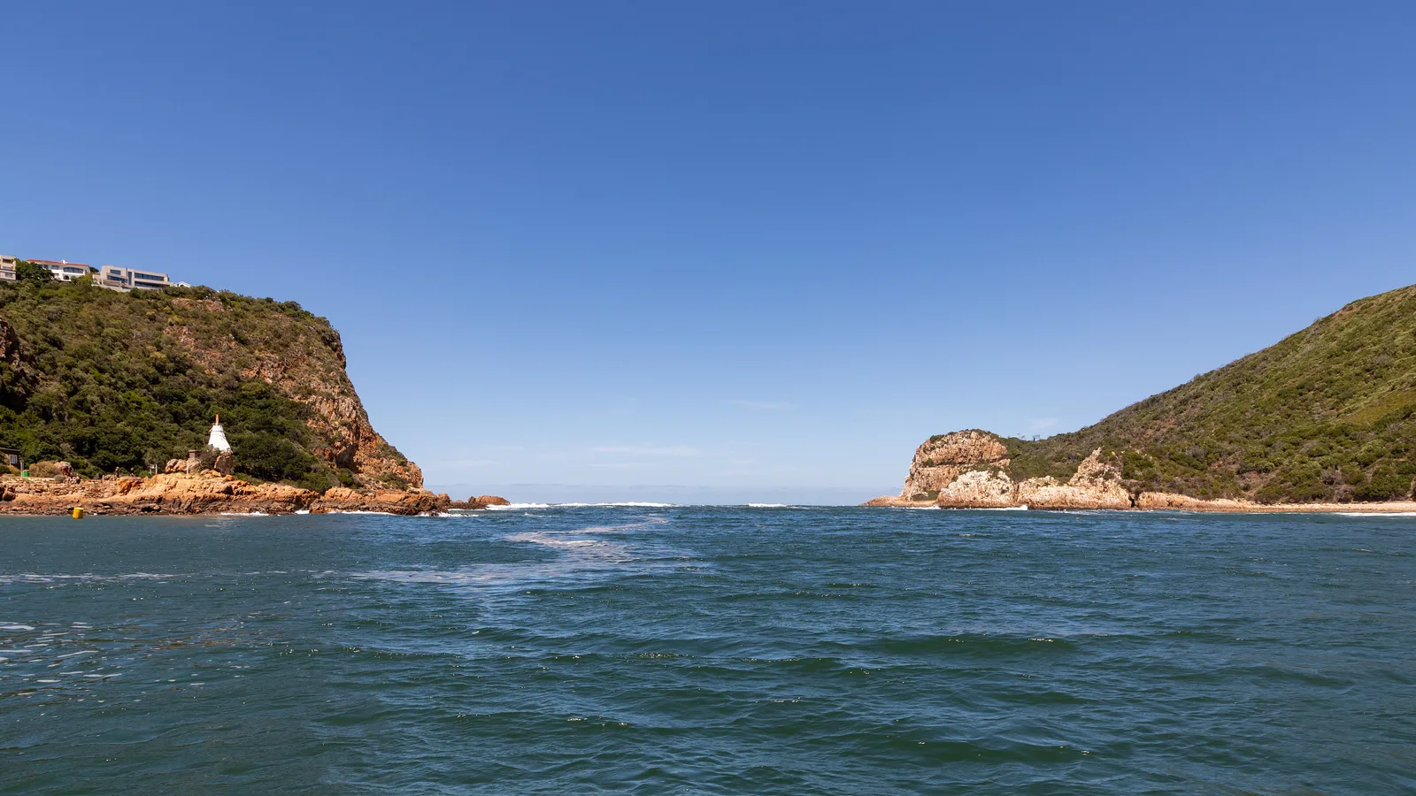 The Knysna Heads — two forested sandstone cliffs framing the channel between the lagoon and the open sea, seen from the water